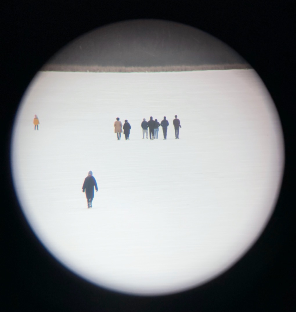 Lab members as seen through a telescope walking on a frozen lake